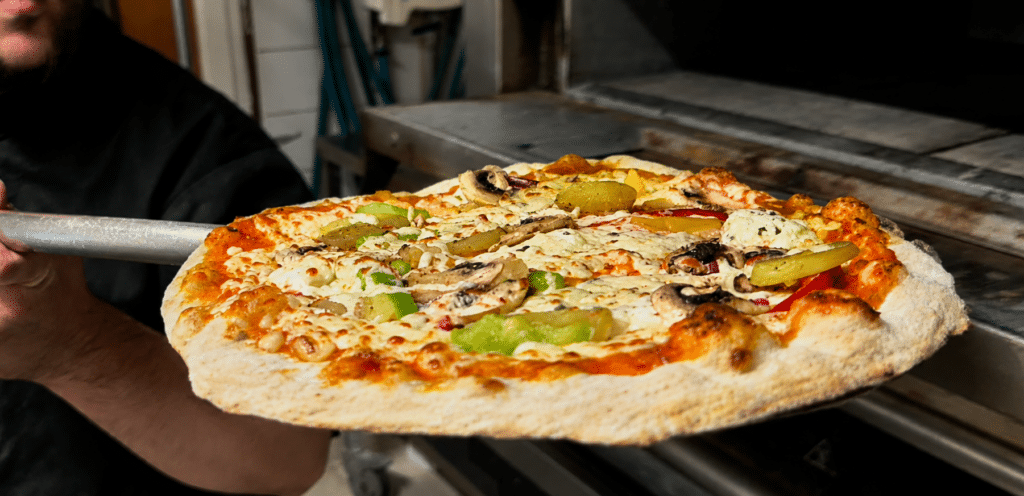 Pizzaiolo sortant du four une pizza aux champignons, poivrons et mozzarella sur sa pelle